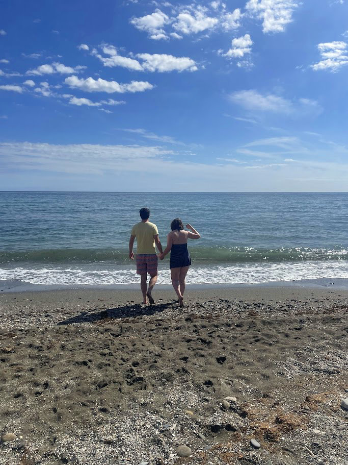 Amy and Gavin on the beach, hand in hand, walking towards the water with their backs to the camera